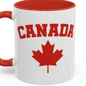 May include: White ceramic mug with a red interior and handle. The mug features the word "CANADA" in red block letters above a red maple leaf design. A patriotic themed mug.