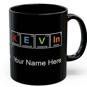 Könnte beinhalten: Schwarze Keramik-Tasse mit dem Namen "KEVIN", der mit Elementen aus dem Periodensystem geschrieben wurde. Die Tasse hat auch den weißen Text "Your Name Here" mit einem weißen Pfeil, der auf den Text zeigt.
