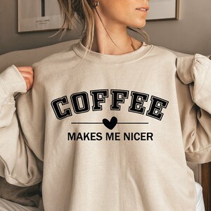 May include: A beige sweatshirt with the text "COFFEE MAKES ME NICER" in black lettering with a small heart between the words.