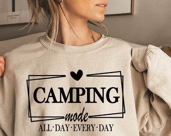 Può includere: Una felpa beige con una grafica nera che dice "Camping mode" con un cuore sopra la parola "Camping" e le parole "All Day Every Day" sotto.