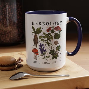 A white mug with a blue handle, featuring illustrations of various plants and flowers, is placed on a wooden surface next to a spoon.