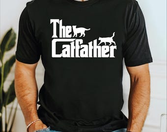 May include: Black t-shirt with the white text "The Catfather" and two cat silhouettes. The design is a parody of the movie "The Godfather". The shirt is a crew neck and short-sleeved.