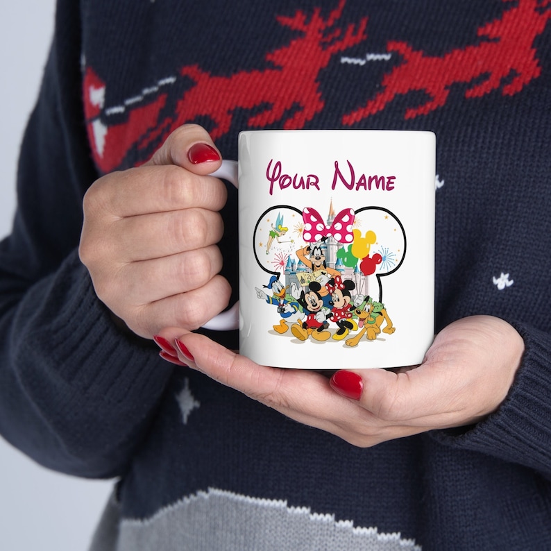 Puede incluir: Taza de cer&aacute;mica blanca con un dise&ntilde;o de personajes de Disney, incluyendo Mickey y Minnie Mouse, el Pato Donald y Goofy. La taza tiene el texto "Your Name" en escritura burdeos. El dise&ntilde;o incluye un lazo rosa y globos coloridos.