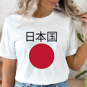 May include: White t-shirt featuring the Japanese flag with a large red circle and black Japanese characters. The shirt is a simple crew neck style.