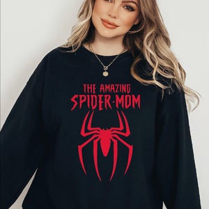 May include: Black sweatshirt with the text "THE AMAZING SPIDER-MOM" in red, along with a red spider graphic. The sweatshirt is a crew neck style.