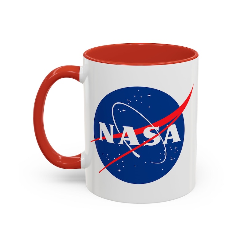 May include: White ceramic mug with a red interior and handle. The mug features the NASA logo in a blue circle with white text and a red swoosh. The mug is designed for hot beverages.