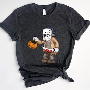 Puede incluir: Una camiseta gris oscuro de manga corta con un gráfico de dibujos animados de un personaje con máscara de hockey blanca, chaqueta beige y pantalones marrones. El personaje sostiene una pequeña calabaza naranja y un cuchillo con sangre.
