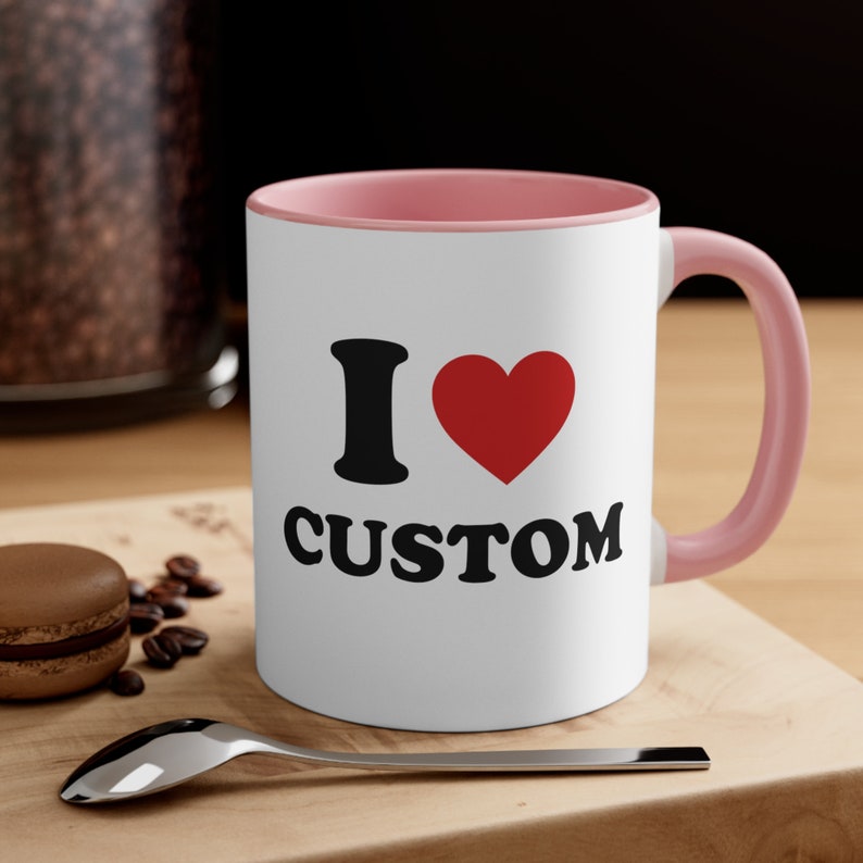 May include: White ceramic mug with a pink rim and handle. The mug has a black and red graphic that says "I &hearts; CUSTOM".