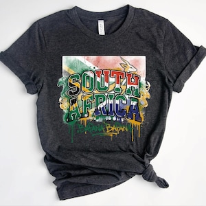 May include: A dark charcoal grey t-shirt featuring a graphic print of the South African flag with a springbok silhouette. The text reads SOUTH AFRICA in bold block letters and BAFANA BAFANA in a stylised script with a paint drip effect below.