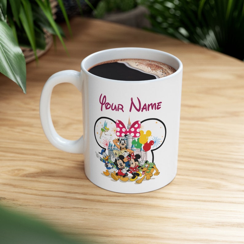 Puede incluir: Taza de cer&aacute;mica blanca con un dise&ntilde;o de personajes de Disney y el texto "Your Name". La taza est&aacute; llena de l&iacute;quido oscuro y tiene un asa blanca. El dise&ntilde;o incluye a Mickey y Minnie Mouse.