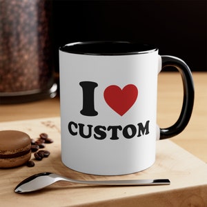 May include: White ceramic coffee mug with a black rim and handle. The mug has a black and red graphic that says "I &hearts; CUSTOM".