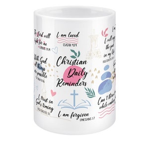 May include: White ceramic mug with a pink and blue design featuring Christian quotes and bible verses. The mug says "Christian Daily Reminders" and includes verses like "I am loved, Isaiah 43:4" and "I am forgiven, Ephesians 1:7".