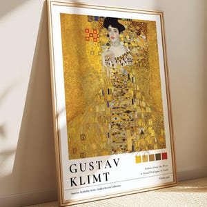 May include: A framed art print featuring Gustav Klimt's "Woman in Gold." The artwork showcases a woman in an ornate gold dress, with the artist's name and artwork title at the bottom. The print is in a light brown wooden frame.
