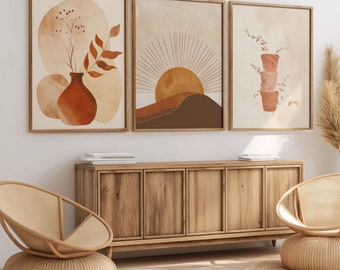 May include: Three abstract art prints in brown, orange, and beige tones. The prints feature a vase with a plant, a sunburst design, and a stack of potted plants. The prints are hanging on a white wall above a wooden cabinet with two chairs.