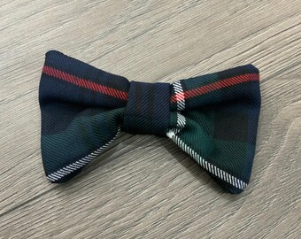 May include: A green, black, and red plaid bow tie. The bow tie is made of a soft, woven fabric.