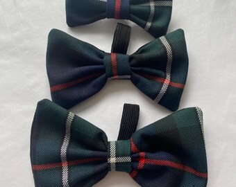 May include: Three plaid bow ties in shades of green, navy, red, and white. Each bow tie has a black elastic band. The bow ties are arranged vertically against a white background.