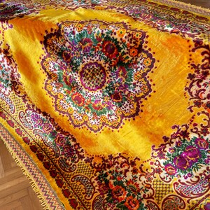 May include: A yellow velvet throw blanket with a floral pattern in shades of red, purple, green, and white. The blanket has a gold fringe border.