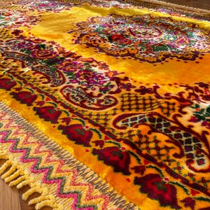 May include: A yellow rug with a floral pattern and a fringe border. The rug has a paisley design and is made of a soft, plush material.