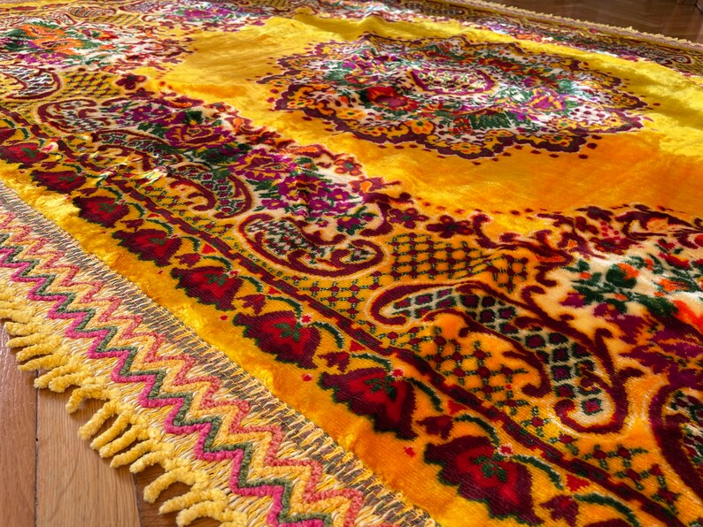 May include: A yellow rug with a floral pattern and a fringe border. The rug has a paisley design and is made of a soft, plush material.
