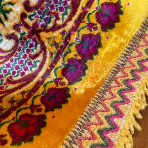 May include: A yellow velvet rug with a floral pattern in shades of red, purple, and green. The rug has a fringed border with a zig-zag pattern in shades of pink, green, and yellow.