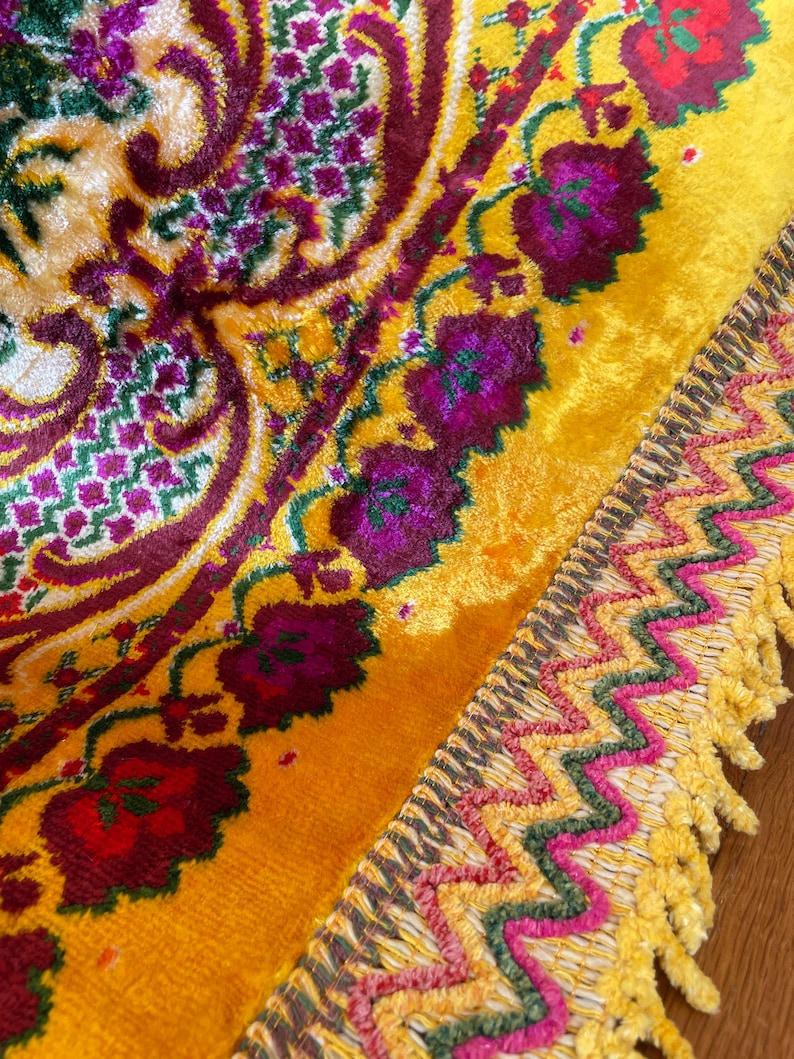 May include: A yellow velvet rug with a floral pattern in shades of red, purple, and green. The rug has a fringed border with a zig-zag pattern in shades of pink, green, and yellow.