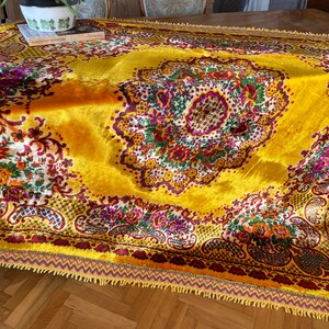 May include: A yellow velvet throw rug with a floral pattern in shades of red, purple, green, and white. The rug has a fringed border.