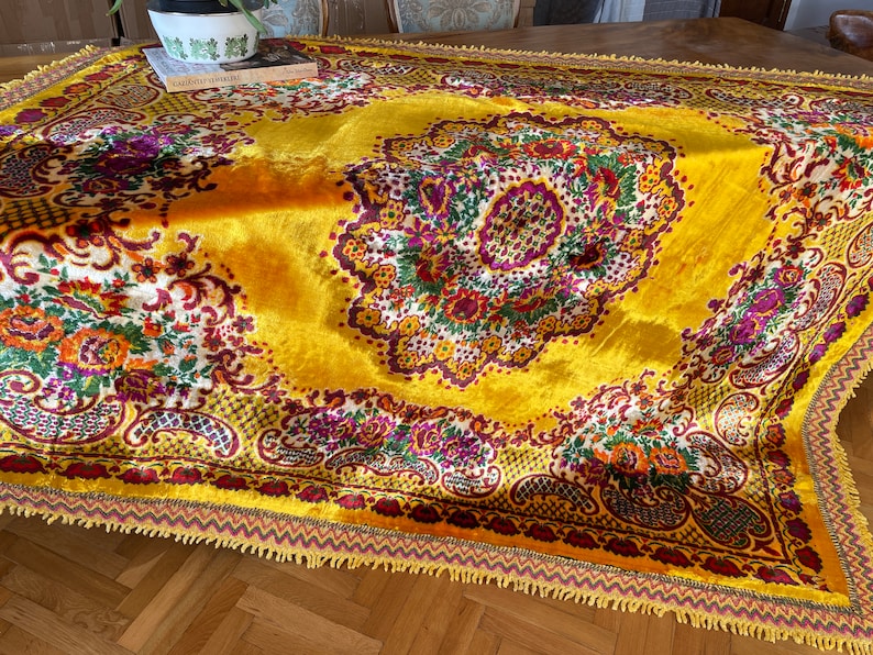 May include: A yellow velvet throw rug with a floral pattern in shades of red, purple, green, and white. The rug has a fringed border.