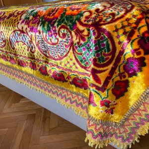 May include: A yellow velvet throw blanket with a colorful floral and paisley pattern. The blanket has a fringed border with gold, pink, and green accents.