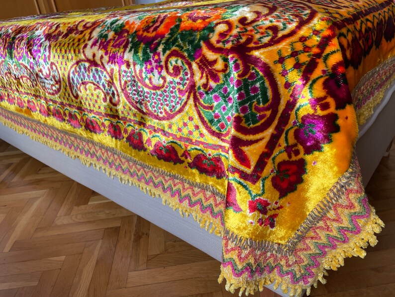 May include: A yellow velvet throw blanket with a colorful floral and paisley pattern. The blanket has a fringed border with gold, pink, and green accents.