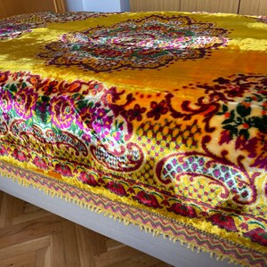 May include: A yellow velvet throw blanket with a colorful floral and paisley pattern. The blanket has a fringed edge.