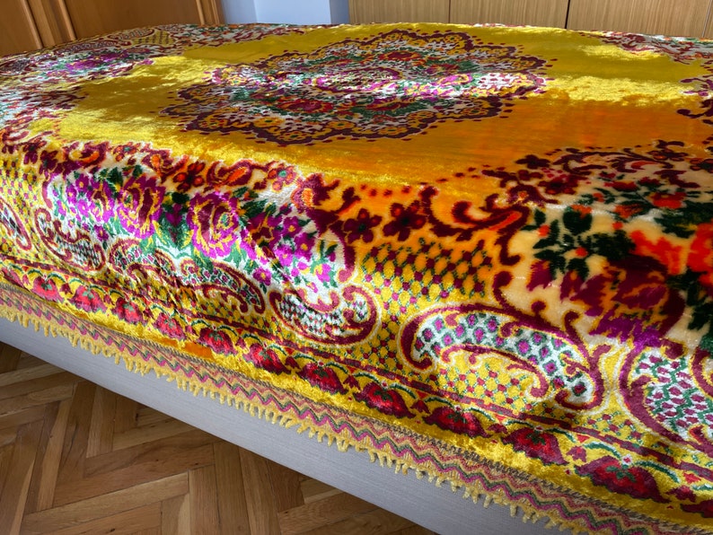 May include: A yellow velvet throw blanket with a colorful floral and paisley pattern. The blanket has a fringed edge.