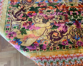 Puede incluir: Primer plano de una alfombra vintage con diseño floral. La alfombra presenta un fondo amarillo con un patrón de flores en tonos rosa, morado, naranja y verde. También se ve una figura de querubín.