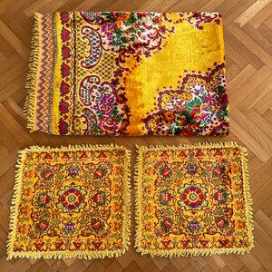 May include: Three yellow throw pillows with a floral pattern and fringe trim. The pillows are on a wooden floor.