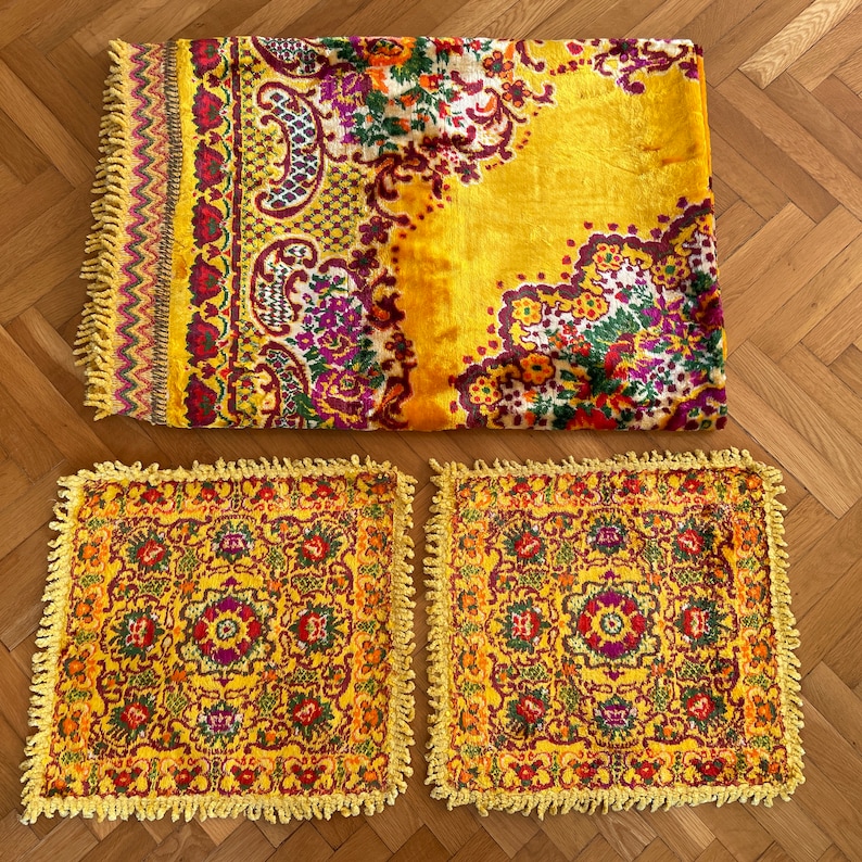 May include: Three yellow throw pillows with a floral pattern and fringe trim. The pillows are on a wooden floor.