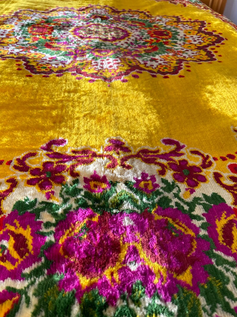 May include: A yellow throw blanket with a floral pattern in shades of pink, green, and white. The blanket has a textured, fuzzy surface.