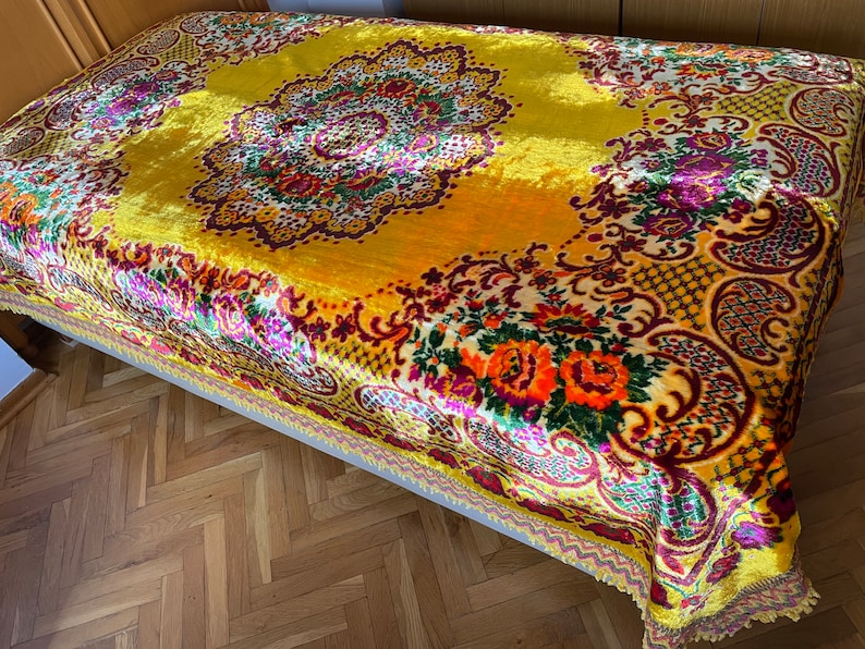 May include: A yellow velvet throw blanket with a floral pattern in shades of red, orange, purple, and green. The blanket has a fringed edge.