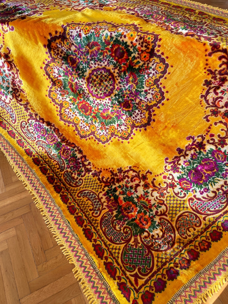 May include: A yellow velvet throw blanket with a floral pattern in shades of red, purple, green, and white. The blanket has a gold fringe border.