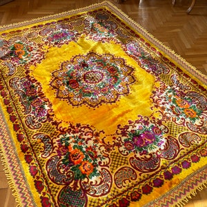 May include: A yellow rug with a floral pattern in shades of red, purple, and green. The rug has a fringed border.