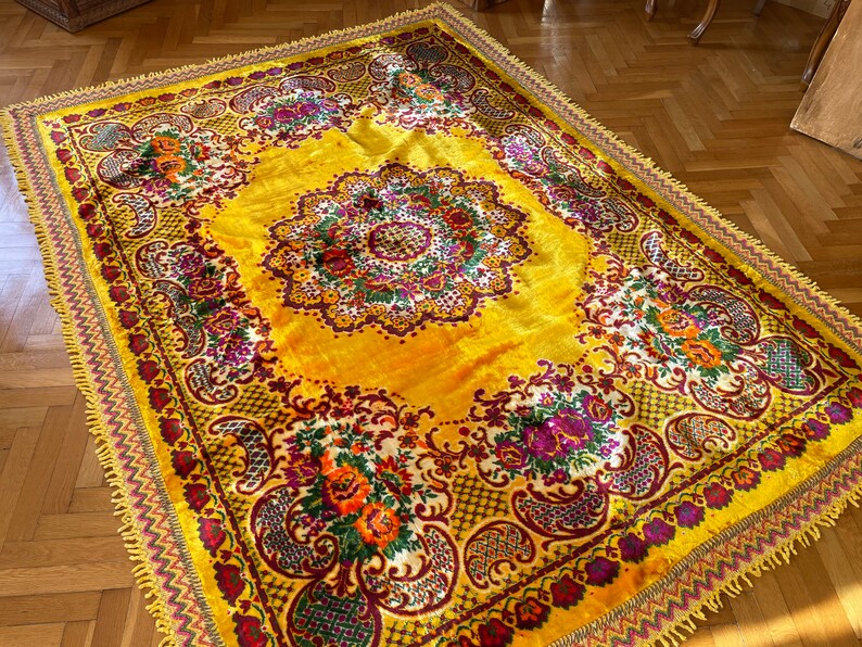 May include: A yellow rug with a floral pattern in shades of red, purple, and green. The rug has a fringed border.