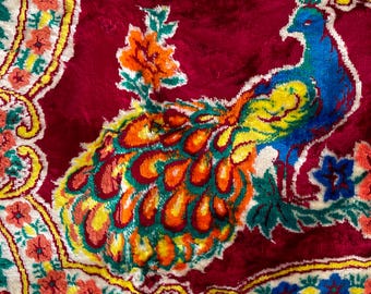Puede incluir: Una manta de terciopelo rojo vintage con un diseño de pavo real colorido. El pavo real está representado en tonos de azul, verde, amarillo y naranja. La manta presenta un patrón de cachemira en el fondo.
