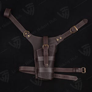 May include: A brown leather holster with adjustable straps for carrying a firearm. The holster has a stitched design and a buckle closure.