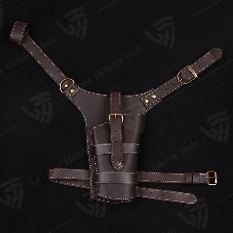 May include: A brown leather holster with adjustable straps for carrying a firearm. The holster has a stitched design and a buckle closure.