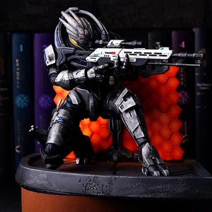 Puede incluir: Figura detallada de un personaje de ciencia ficción en posición de rodillas, sosteniendo un rifle futurista. La figura está vestida con una armadura oscura con detalles plateados, sobre un fondo de libros y un patrón hexagonal naranja brillante.