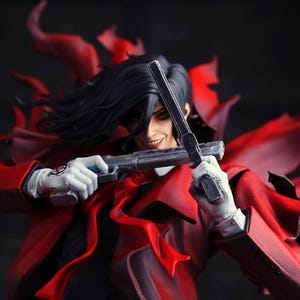 May include: A detailed figurine of a character in a red coat, black suit, and white gloves, holding two silver pistols. The figure has black hair and a sinister smile. The background is dark.