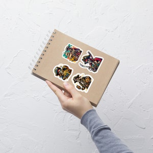 Könnte beinhalten: Ein Set mit vier Piraten-Schädel-Stickern, die einen Skelett-Piraten mit einer Schatztruhe, einen Skelett-Piraten mit einer Flasche Rum, einen Skelett-Piraten mit einem Schwert und einen Skelett-Piraten mit einem Schädel zeigen. Die Sticker befinden sich auf einem braunen Notizbuch.