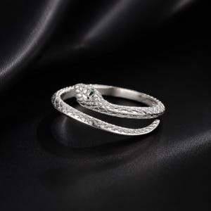 May include: A silver-toned wrap ring shaped like a coiled snake. The metal surface features a textured, scale-like pattern across the entire band. The head of the snake is detailed with small indentations and a tiny, dark green accent stone.