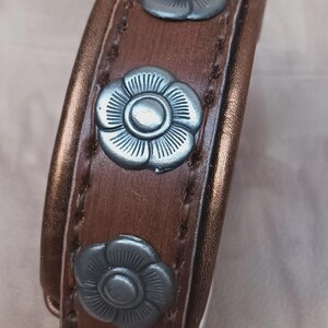 May include: A brown leather bracelet with three silver flower-shaped accents.