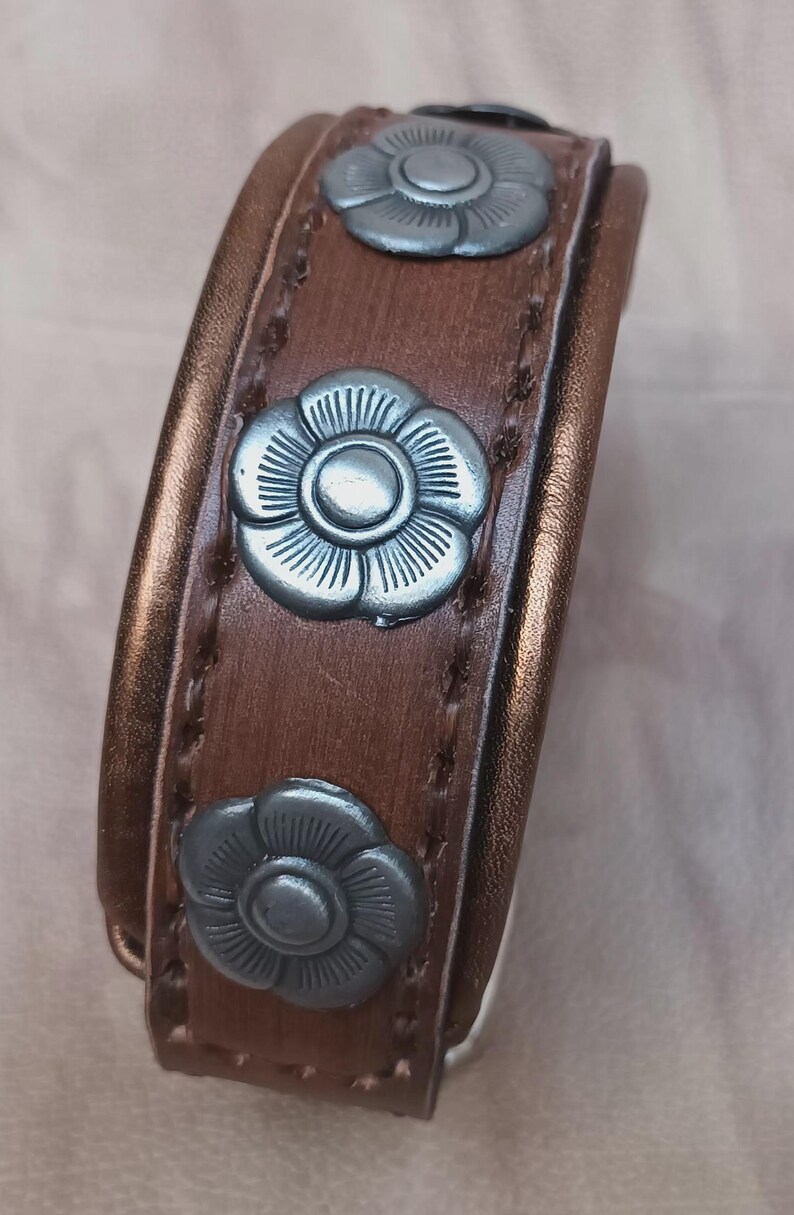 May include: A brown leather bracelet with three silver flower-shaped accents.
