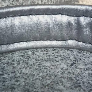 Puede incluir: Primer plano del acolchado de la diadema de unos auriculares de color plateado. La diadema est&aacute; hecha de un material suave y acolchado y tiene una costura cosida.
