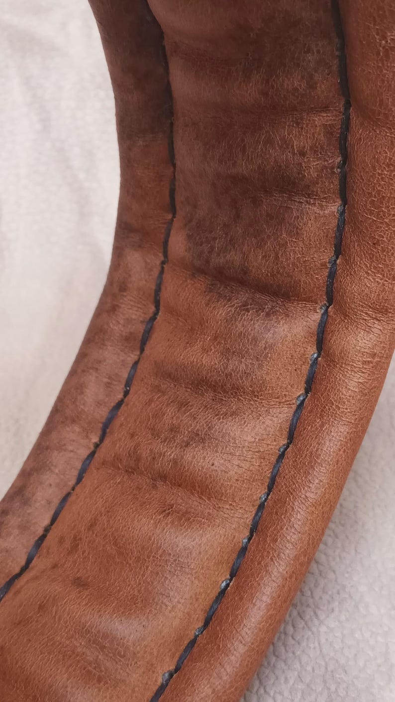 May include: Close-up of brown leather with a black stitched seam. The leather has a textured surface.